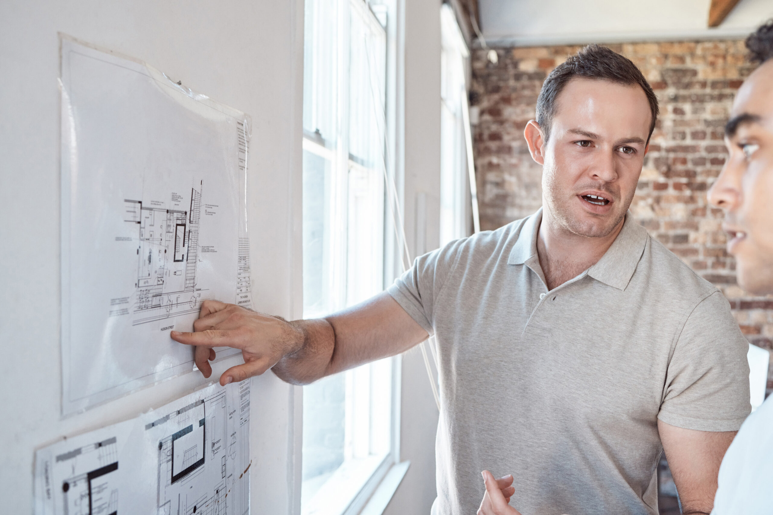 Two men pointing at architectural drawings on a white board