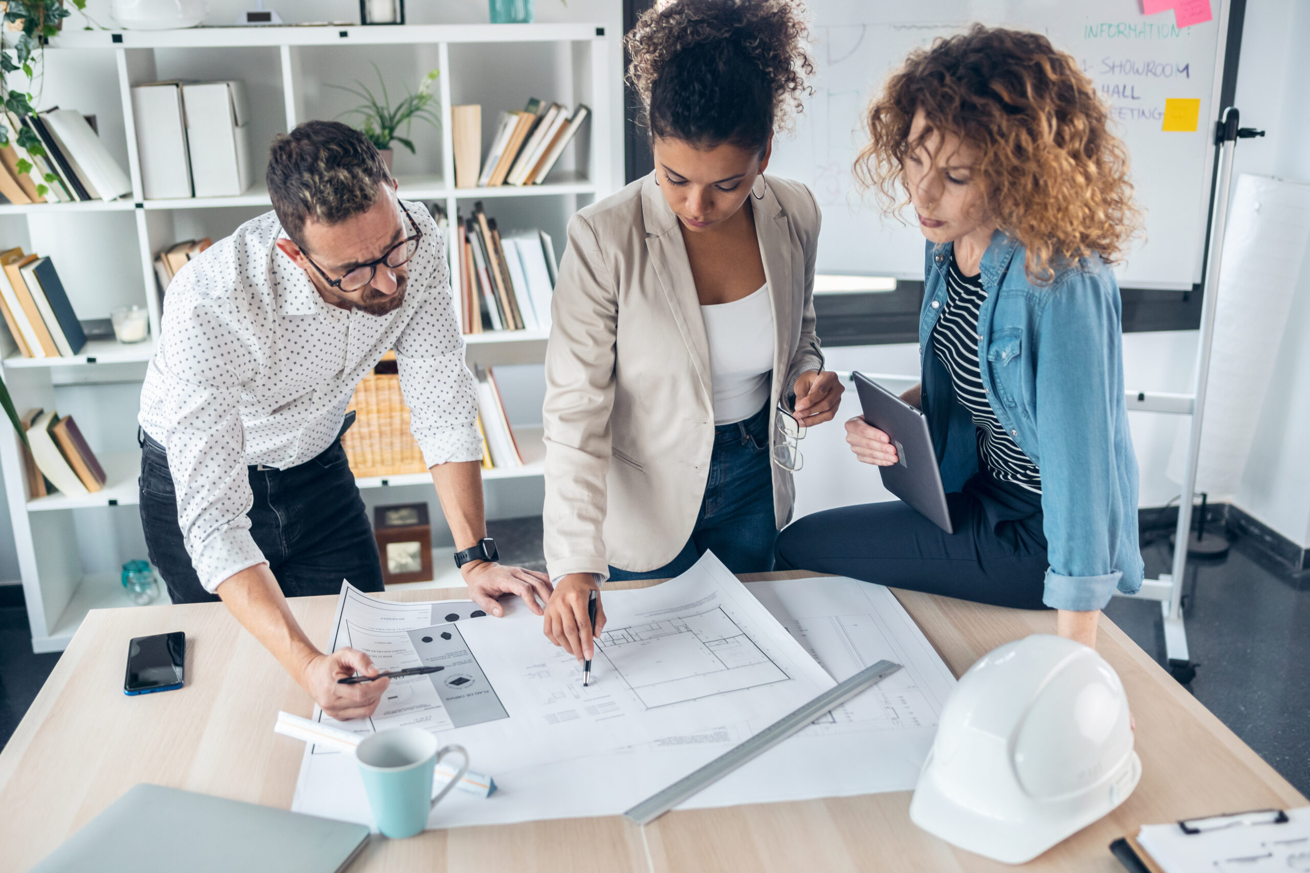Man and two women looking at building drawings on a table discussing the building project